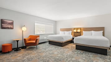 A hotel room with two beds, a chair, a small table, a lamp, and a window with a view.