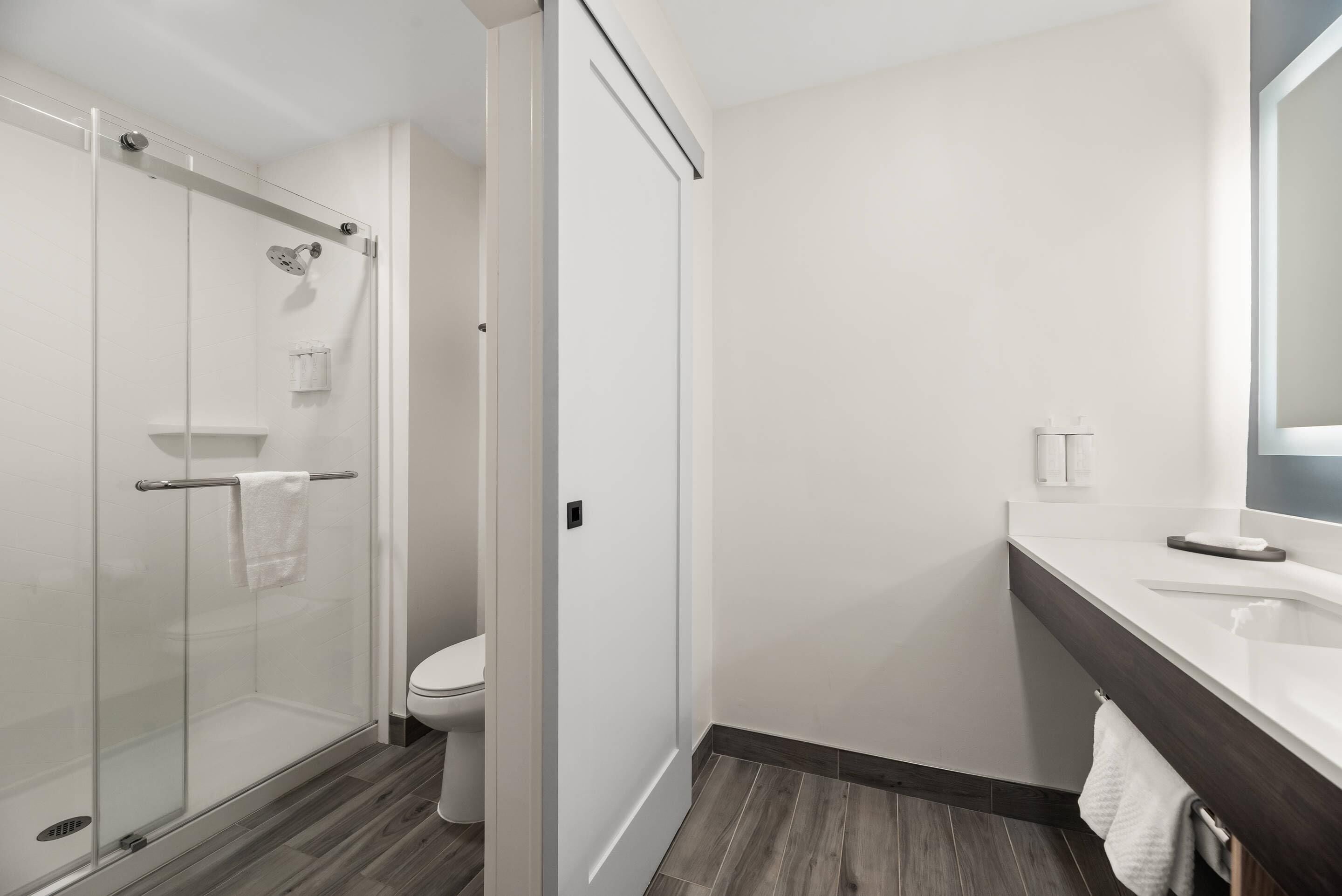 A modern bathroom with a glass shower enclosure, a white toilet, and a dark wood floor.