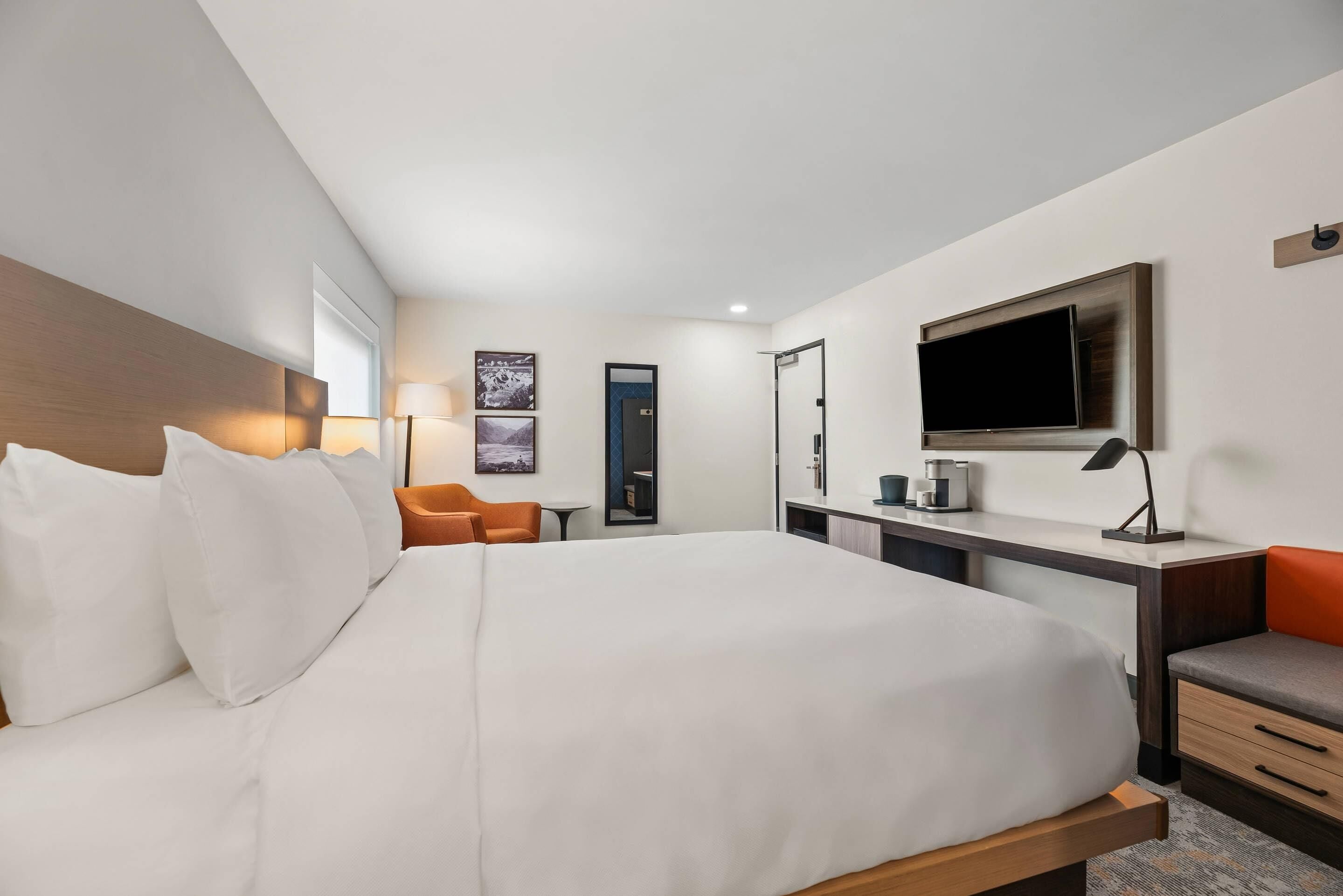 Habitación de hotel con una cama grande, un escritorio con televisión de pantalla plana, una silla y una mesita.