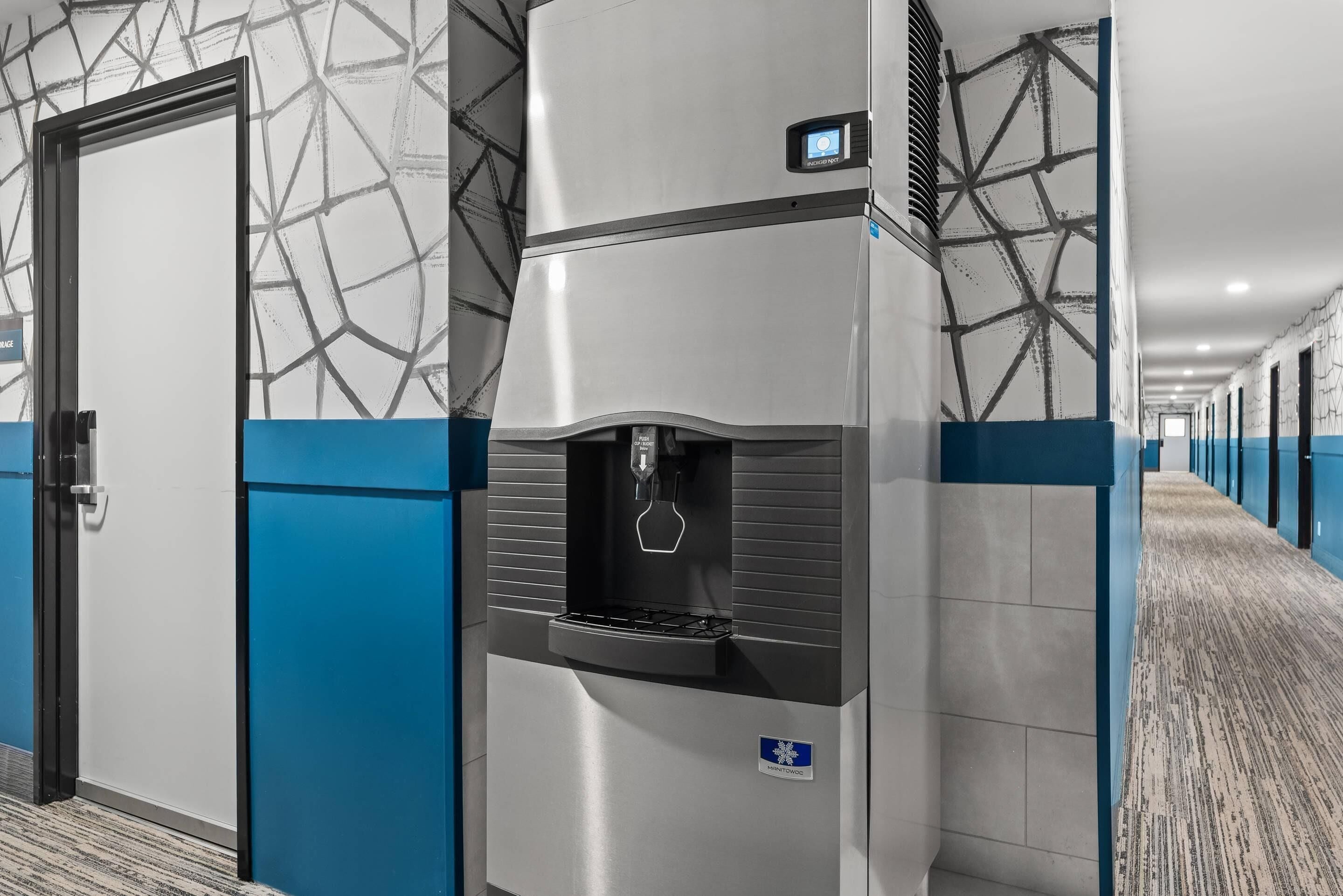A modern hotel corridor with a water dispenser, a door, and patterned walls.
