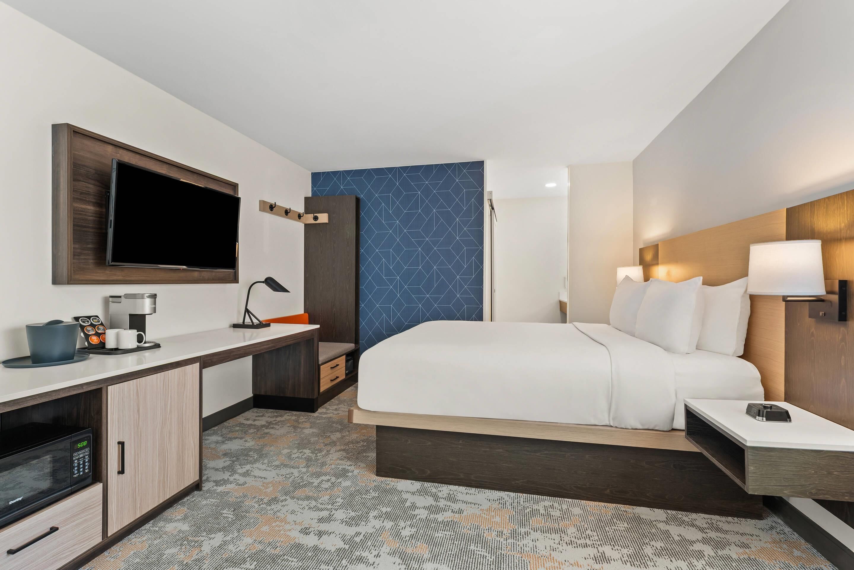 A hotel room with a bed, a desk with a flat-screen TV, a coffee maker, and a microwave.