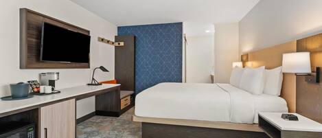 Habitación de hotel con cama, escritorio, televisor de pantalla plana, cafetera y microondas.