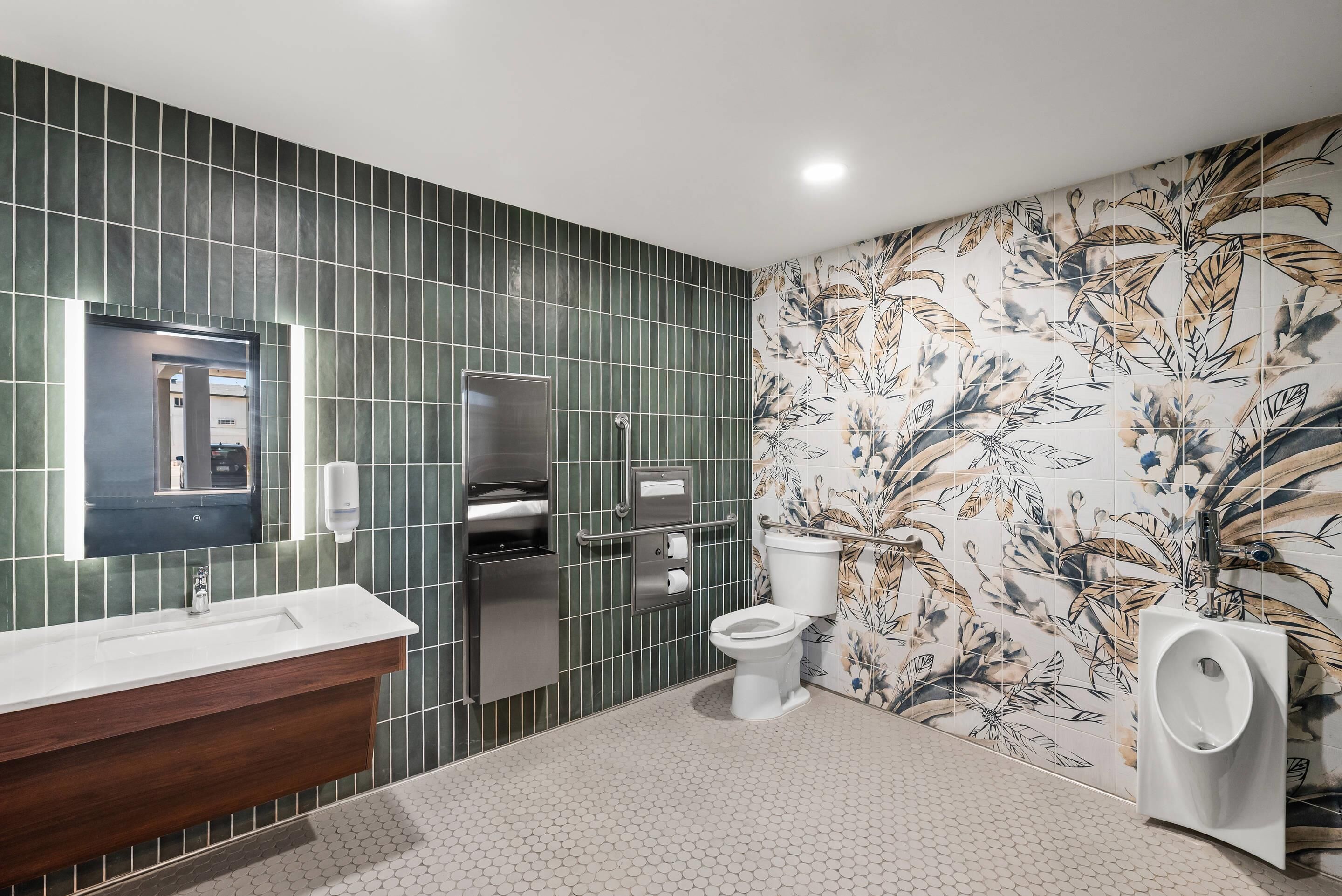 A modern bathroom with a large mirror, a wooden vanity, a toilet, and a urinal.