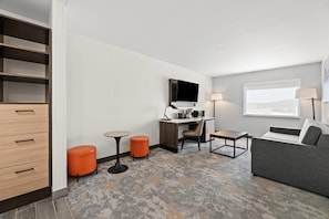 Quarto de hotel com uma mesa, uma televisão, um sofá e uma pequena mesa.