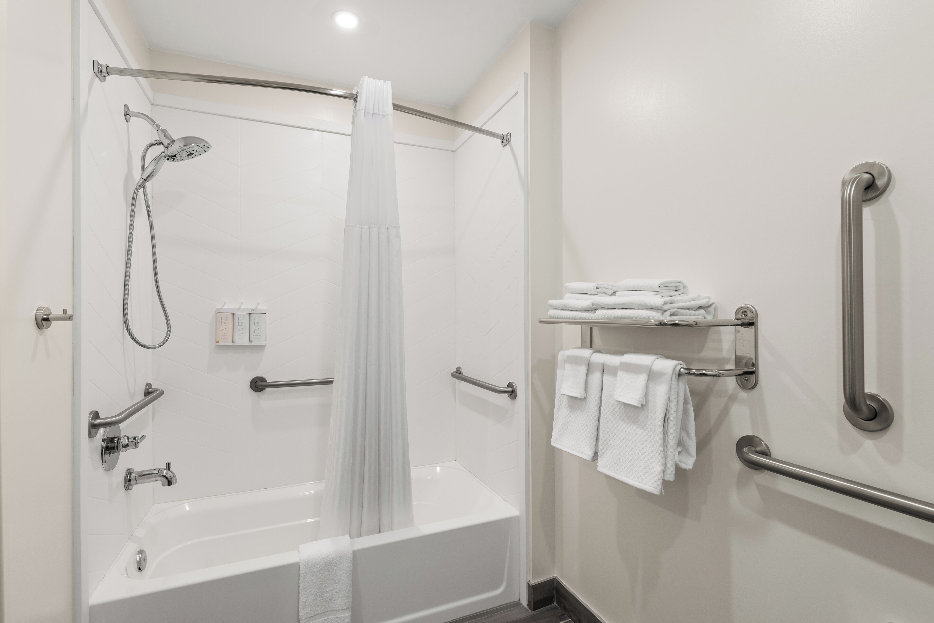 Un baño moderno con cabina de ducha, barras de apoyo, una bañera blanca y toallas ordenadas.