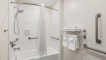 Un baño moderno con cabina de ducha, barras de apoyo, una bañera blanca y toallas ordenadas.
