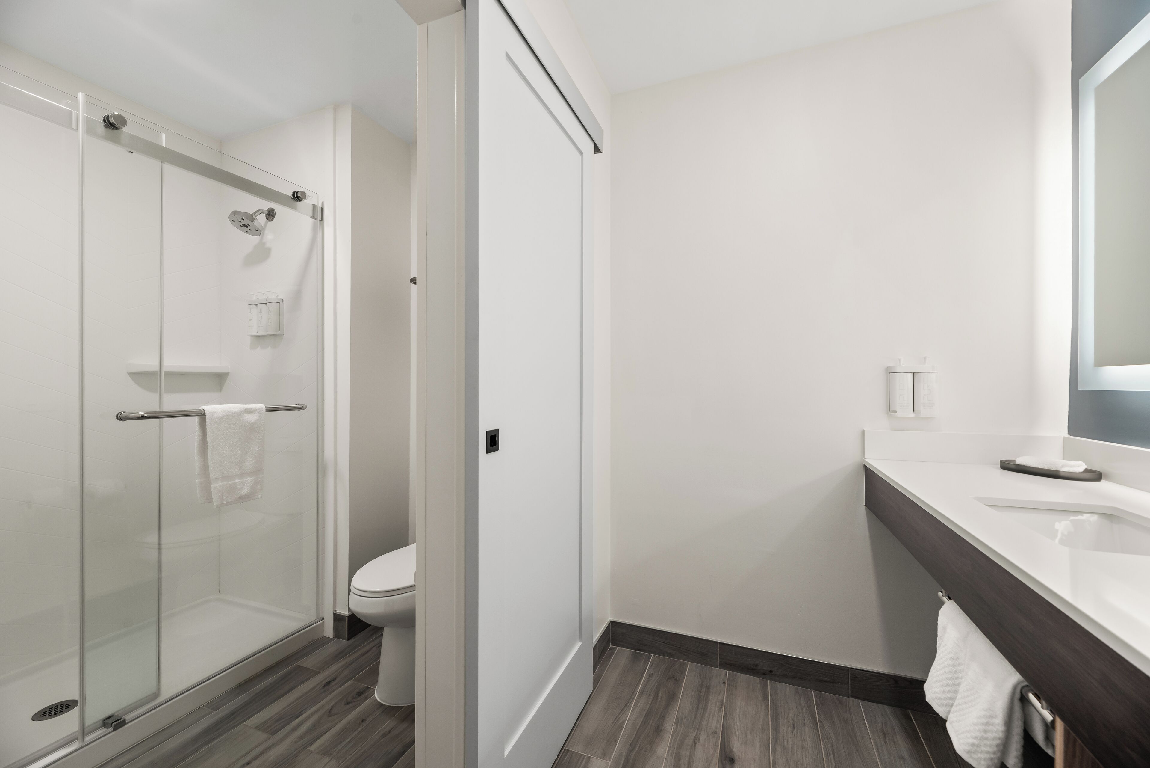 A modern bathroom with a glass shower enclosure, a toilet, and a sink with a dark countertop.