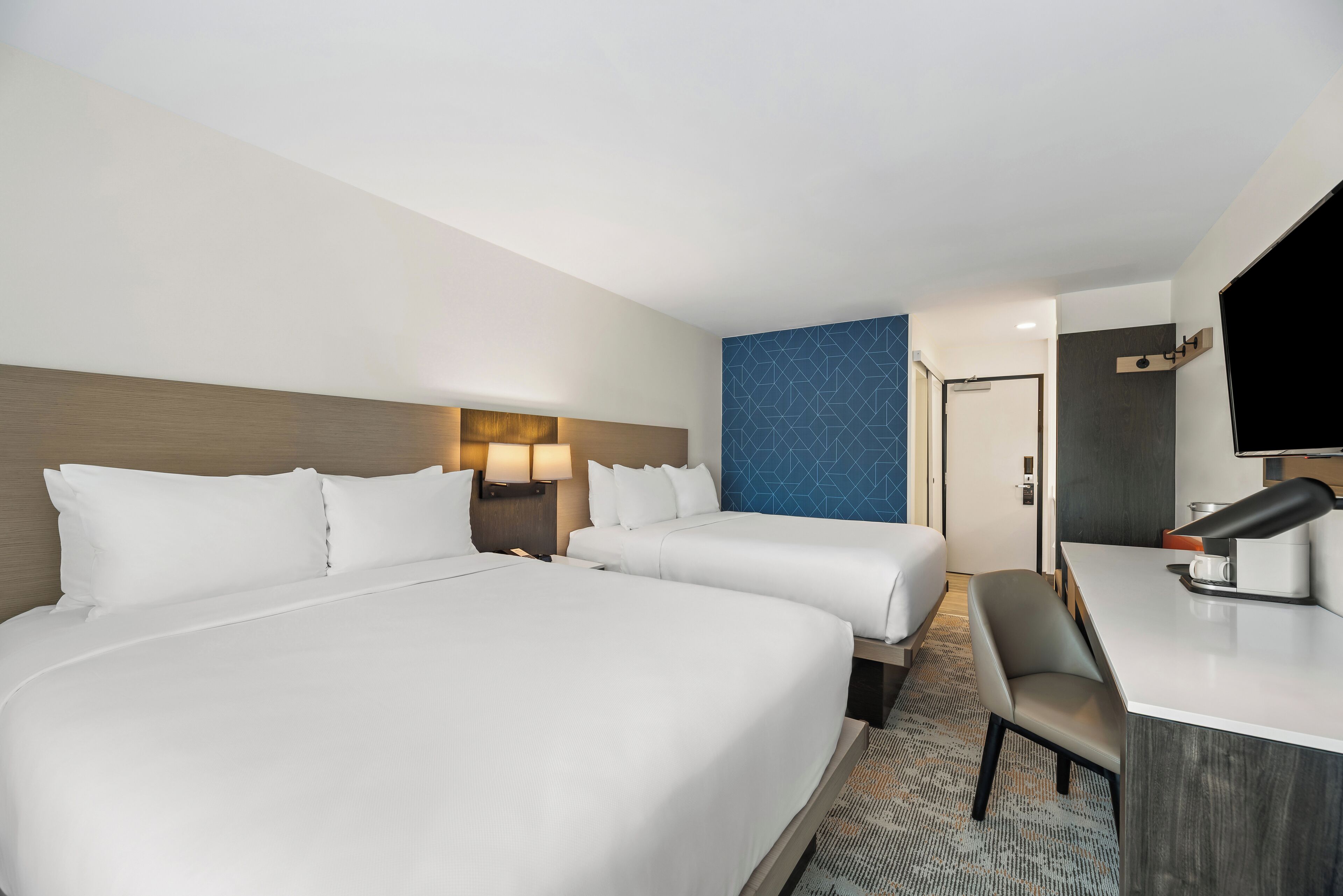 A hotel room with two beds, a desk, a chair, and a television.