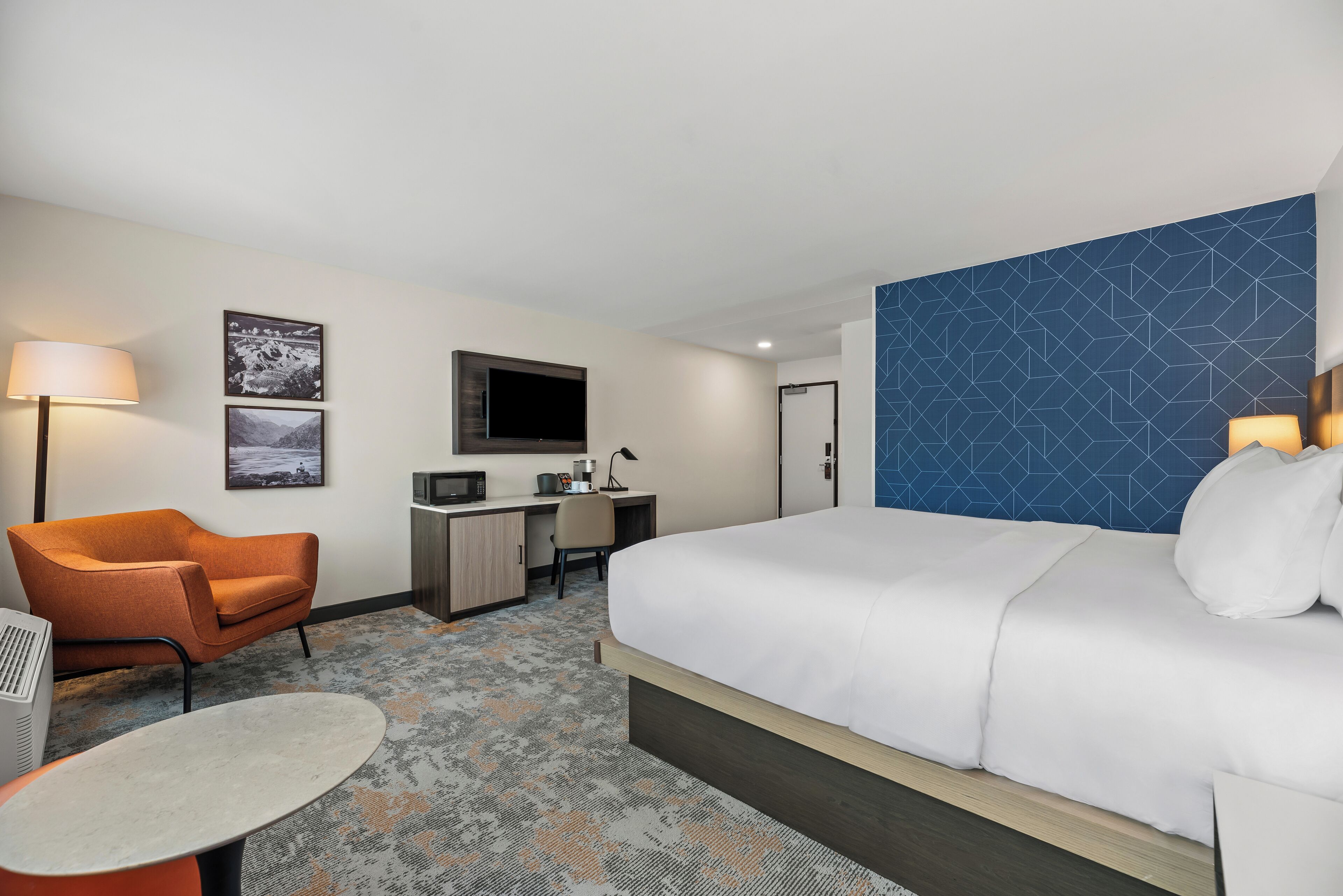 A hotel room with a bed, a desk, a chair, a TV, and a lamp.