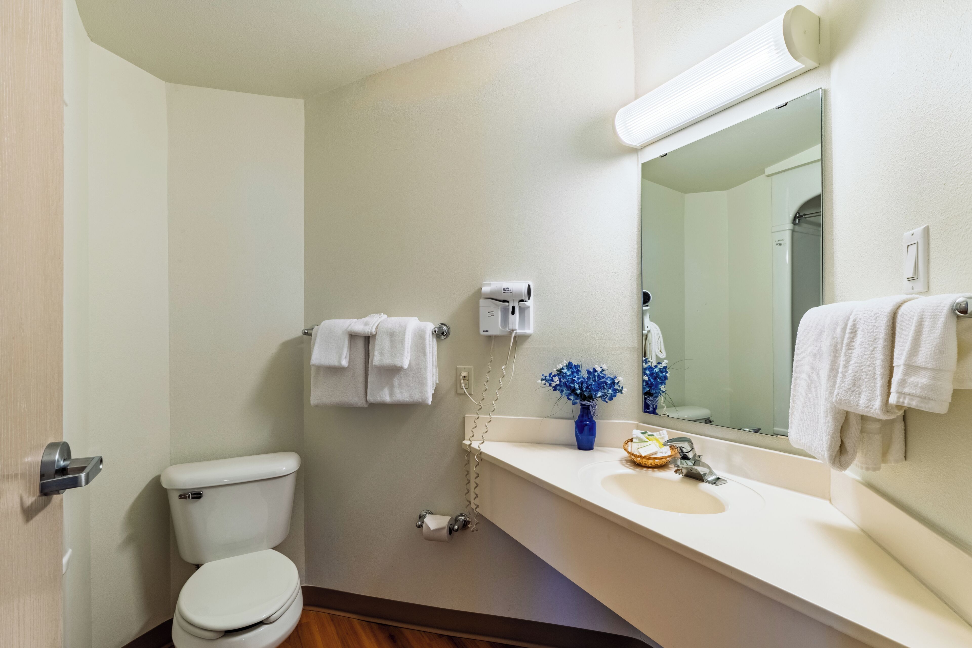 Baño con inodoro, lavamanos, espejo, toallero y secador de pelo.