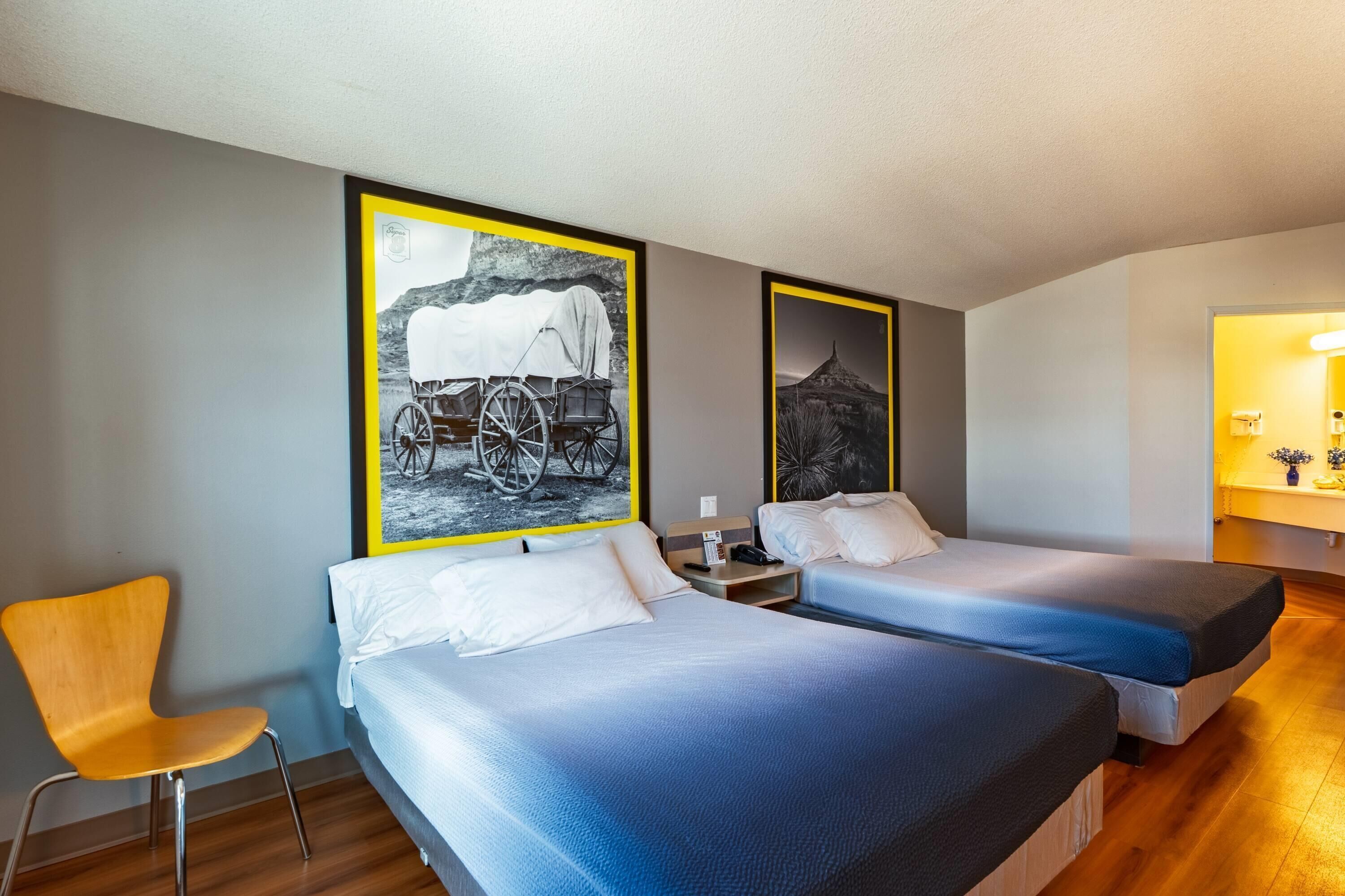 Een hotelkamer met twee bedden, een stoel en een groot, ingelijst schilderij aan de muur.