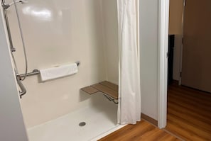 A shower with a towel rack, a small shelf, and a shower curtain. - Super 8 by Wyndham Sidney NE (Sidney)