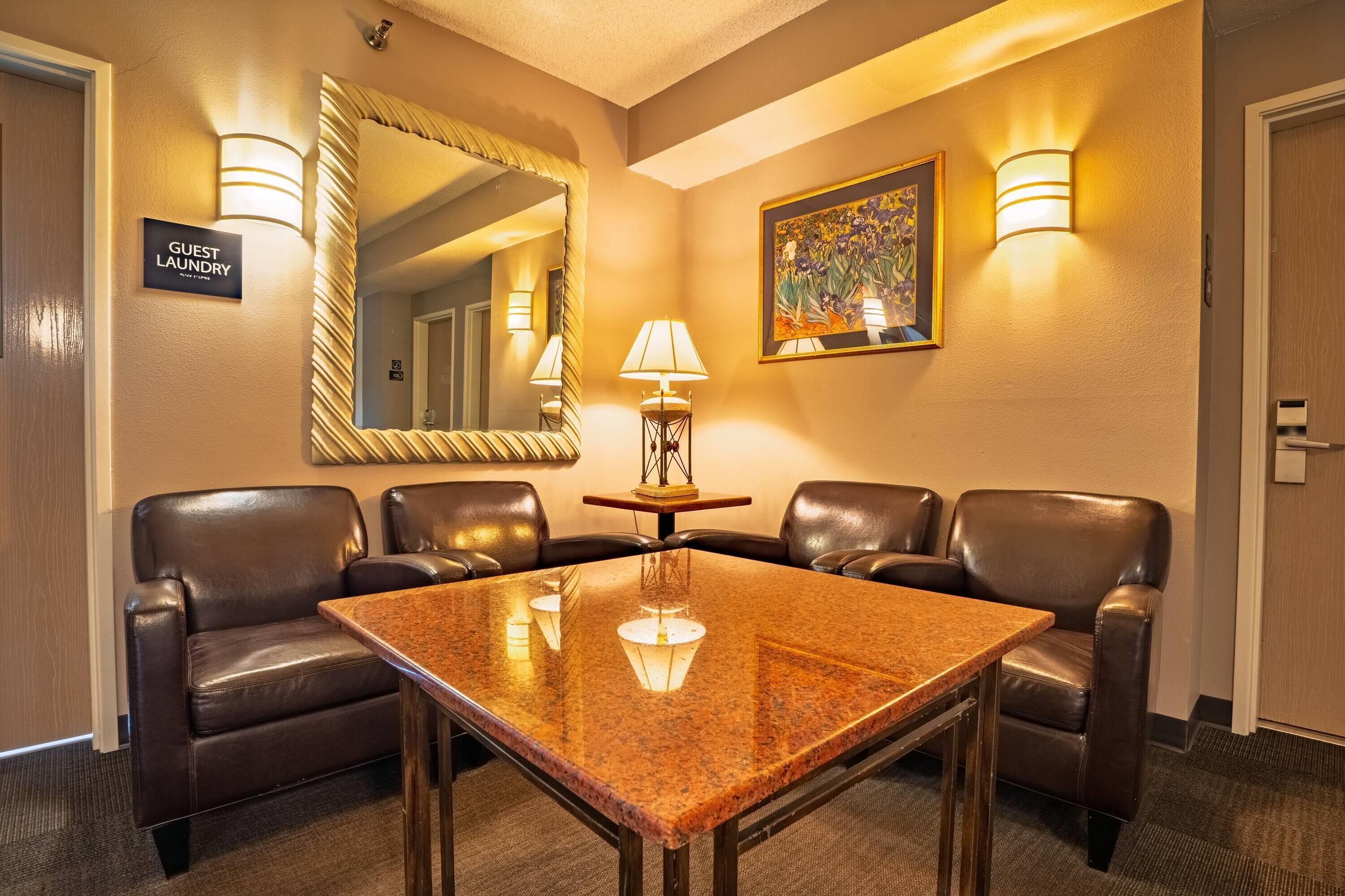 A hotel room with a marble table, leather chairs, a mirror, wall-mounted lights, and a painting.