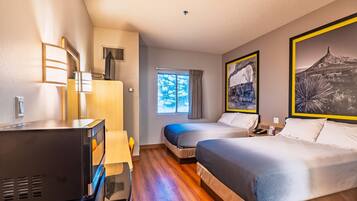 A hotel room with two beds, a desk with a television, a window with curtains, and artwork on the walls.
