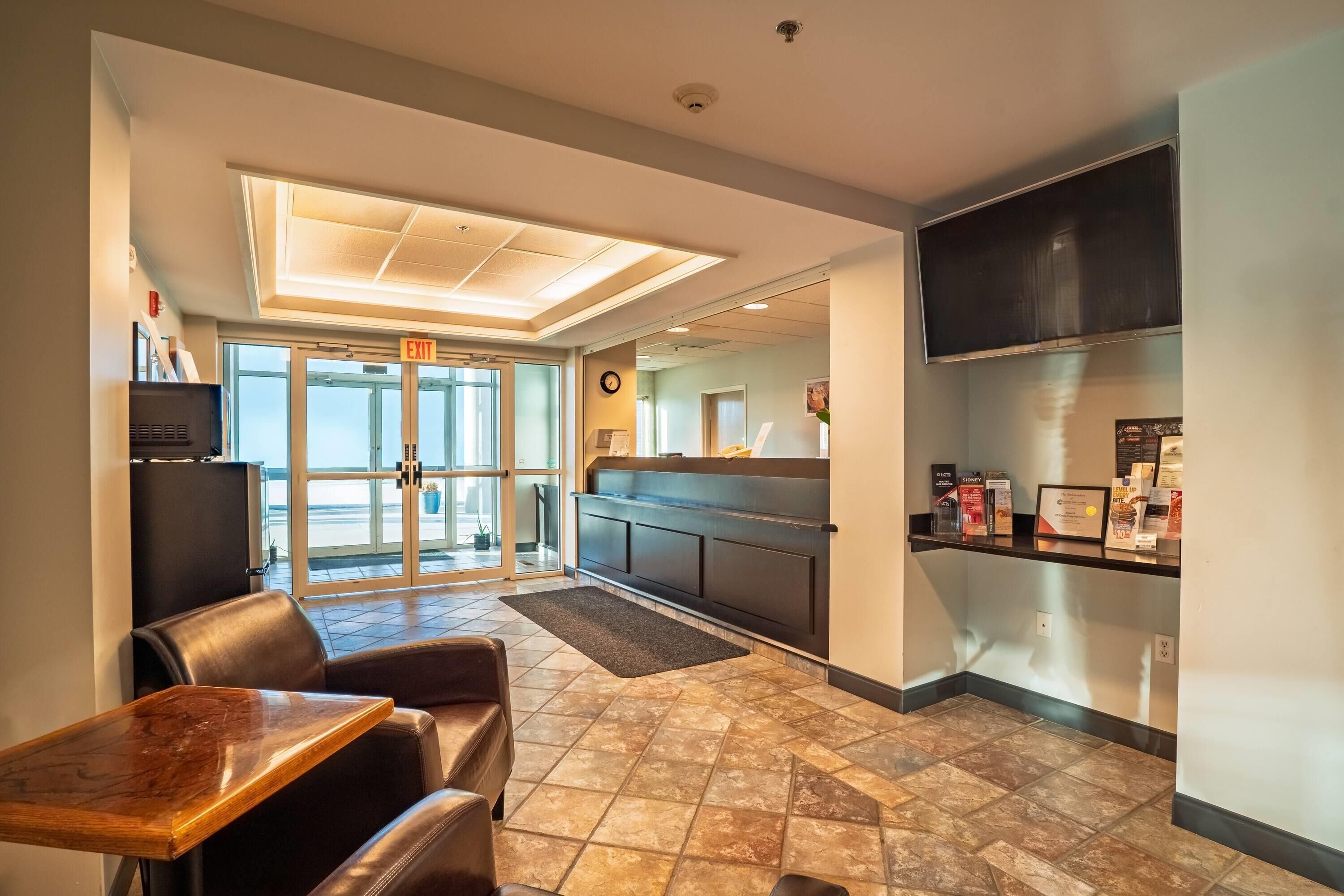 A hotel lobby with a reception desk, seating area, and a view through the glass doors.