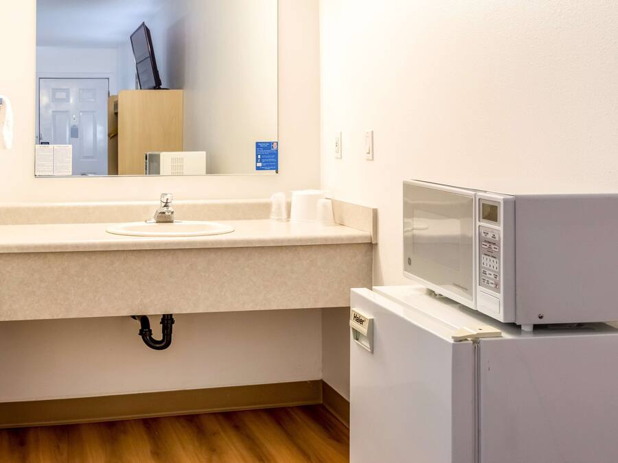 A hotel bathroom with a sink, mirror, and a microwave on a small white cabinet.