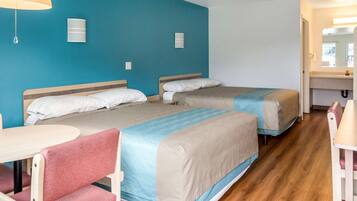 A hotel room with two beds, a small table, a chair, and a bathroom with a mirror.
