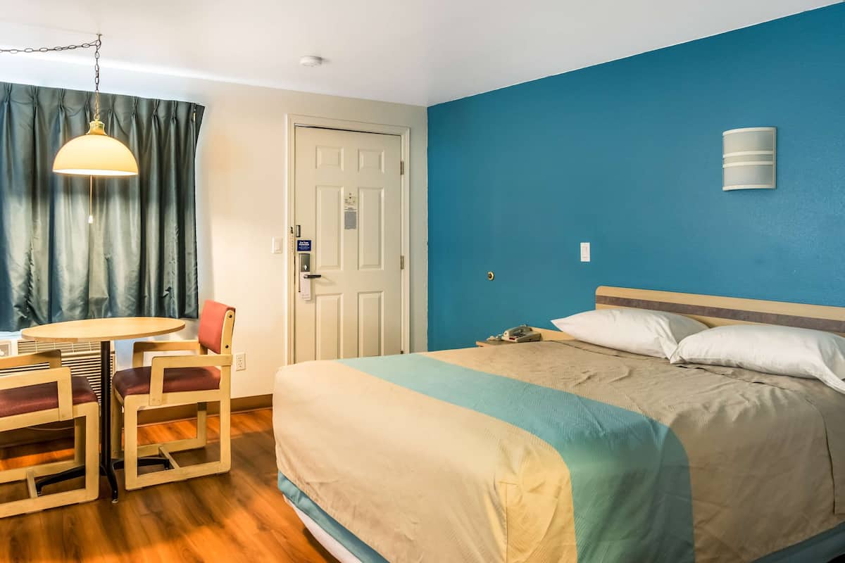 A hotel room with a bed, a desk with two chairs, a hanging lamp, and a door.