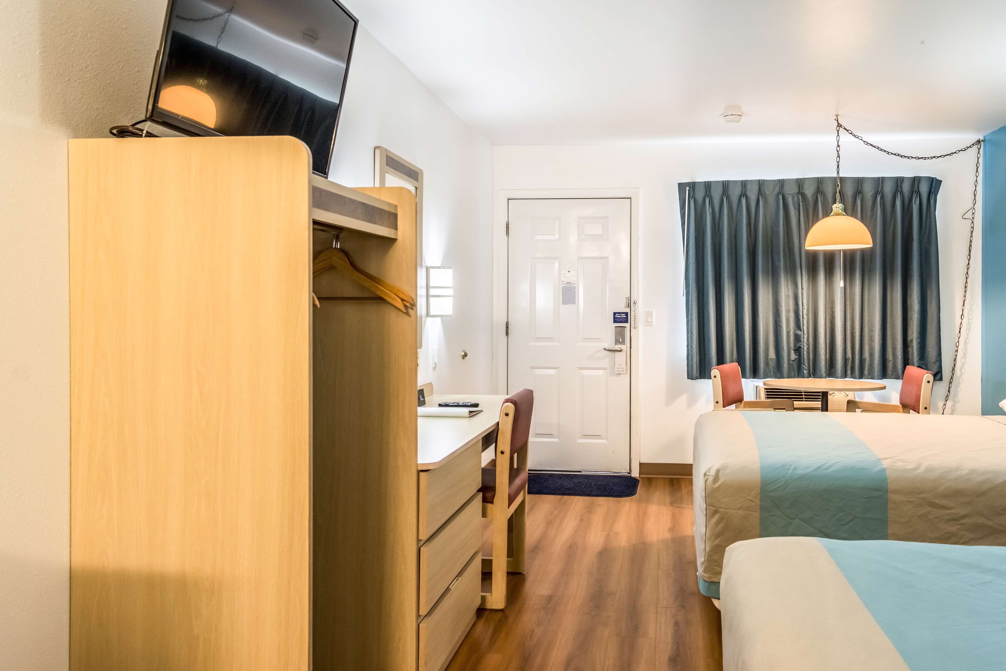 A hotel room with a desk, chair, bed, and a TV on a wooden cabinet.