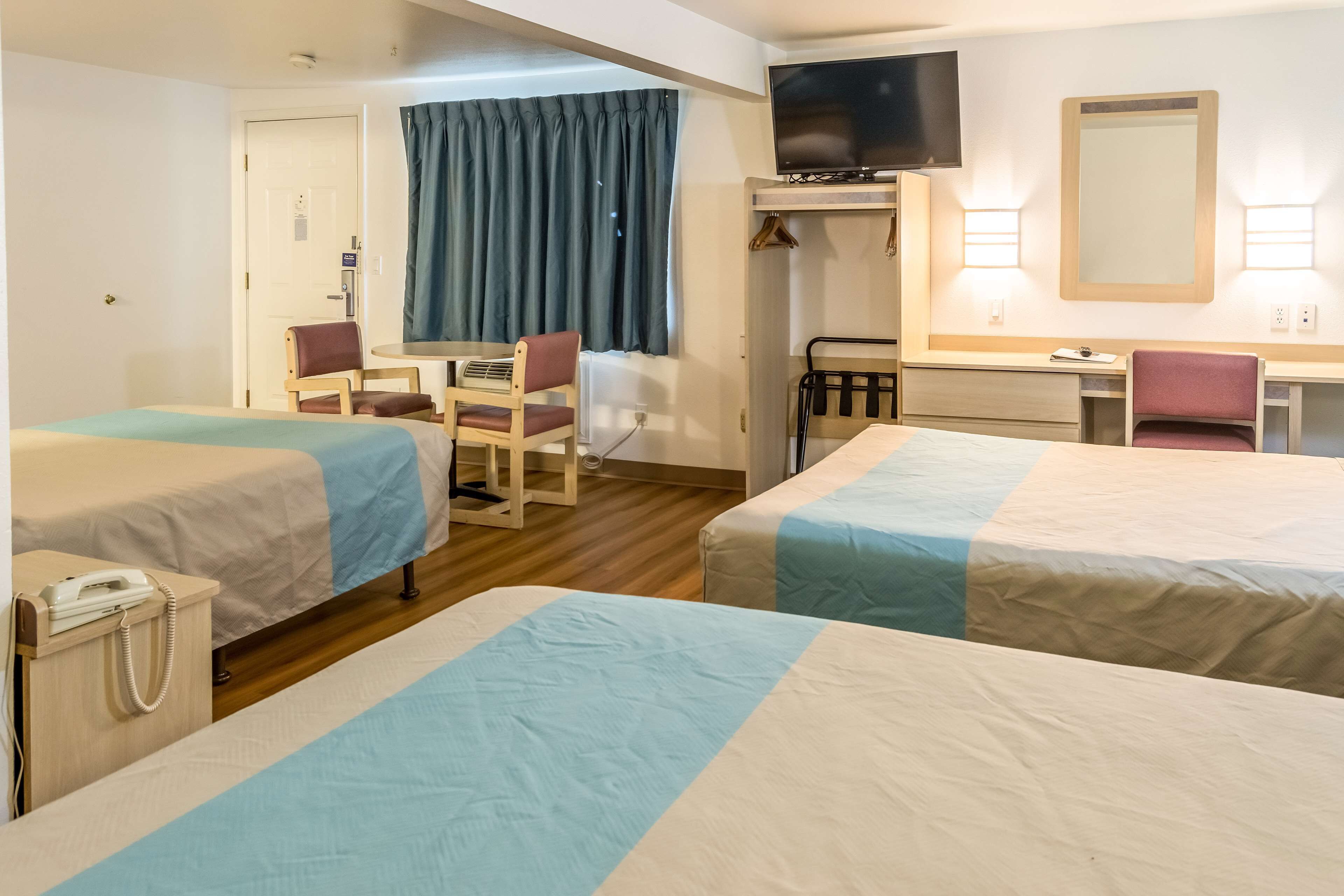 A hotel room with two beds, a desk, a chair, a television, and a mirror.