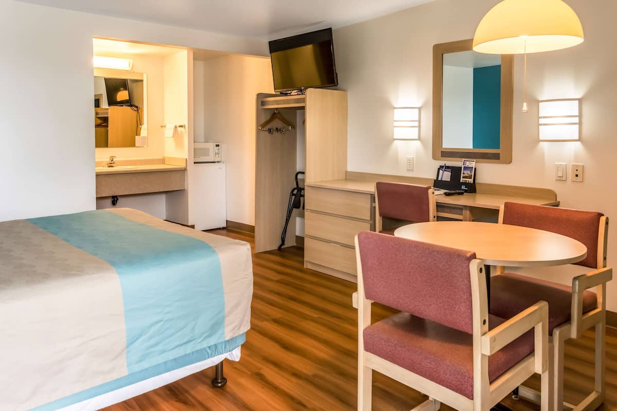 A hotel room with a bed, a desk, a chair, a television, a mirror, and a wardrobe.