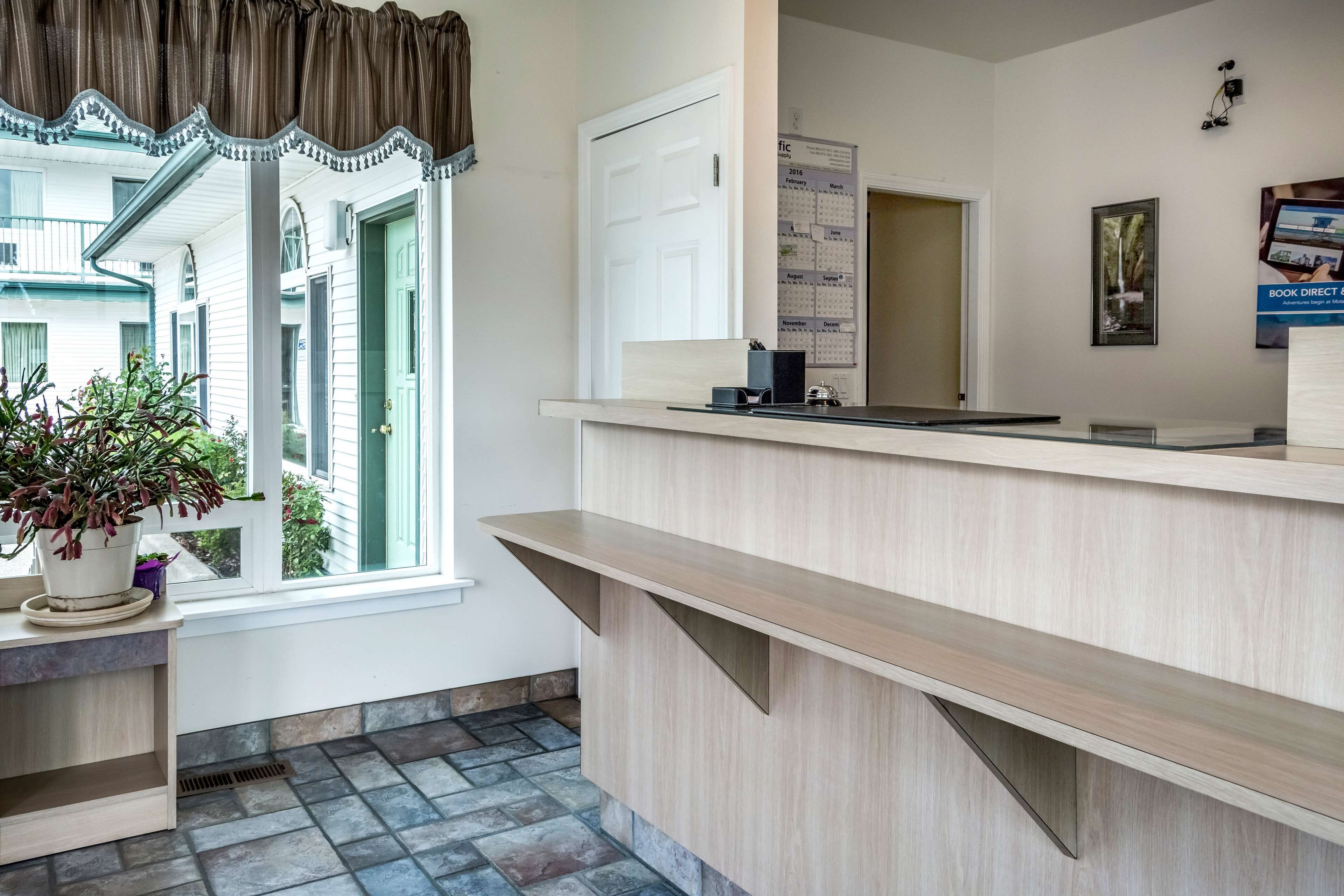 A reception area with a wooden counter, a potted plant, a calendar, and a door leading to another room.