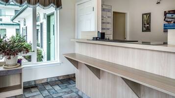 A reception area with a wooden counter, a potted plant, a calendar, and a door leading to another room.