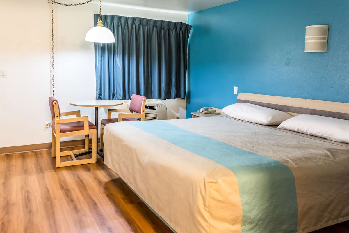 A hotel room with a bed, a desk, a chair, a table, and a ceiling fan.