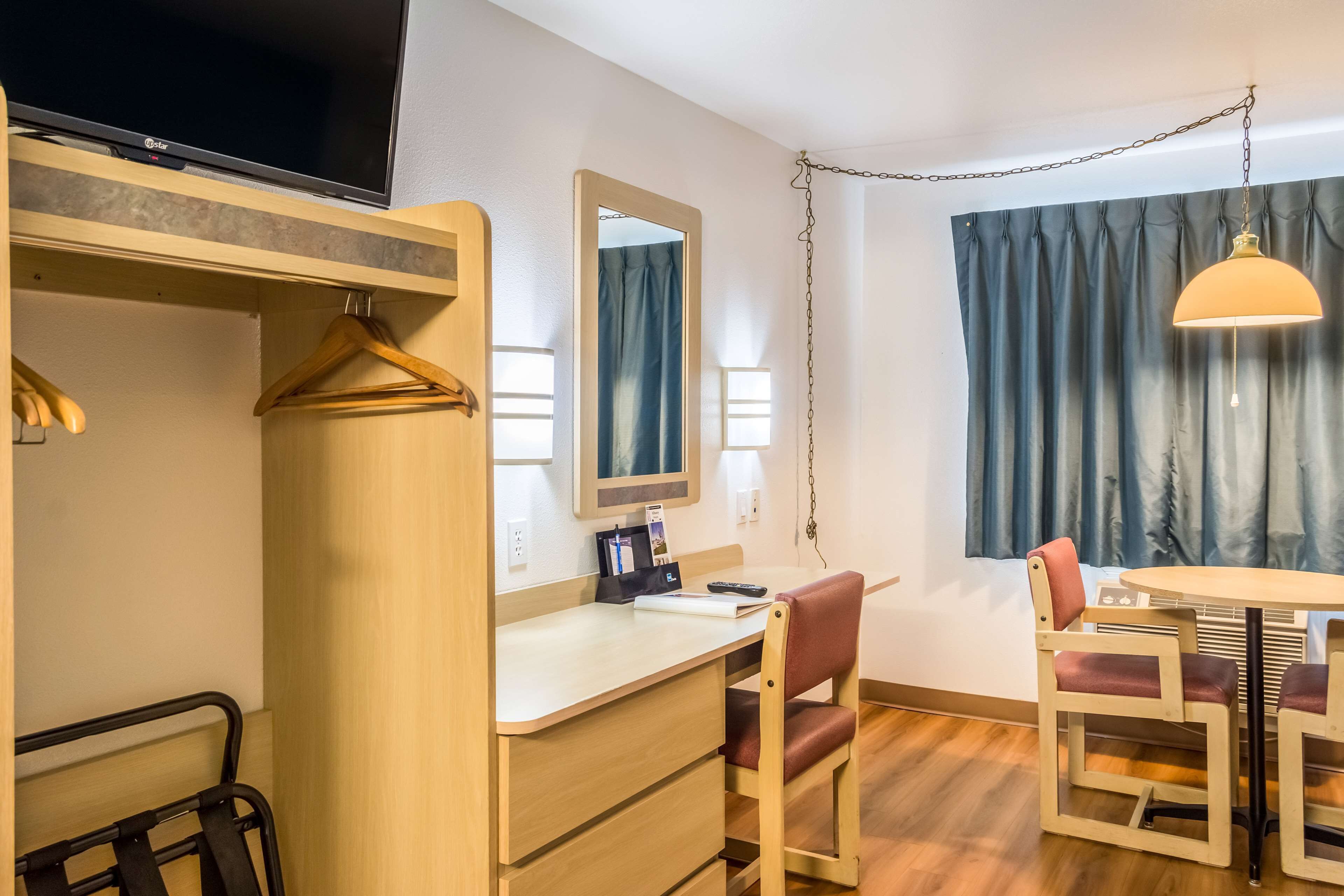 A hotel room with a desk, chair, and a TV mounted on the wall.