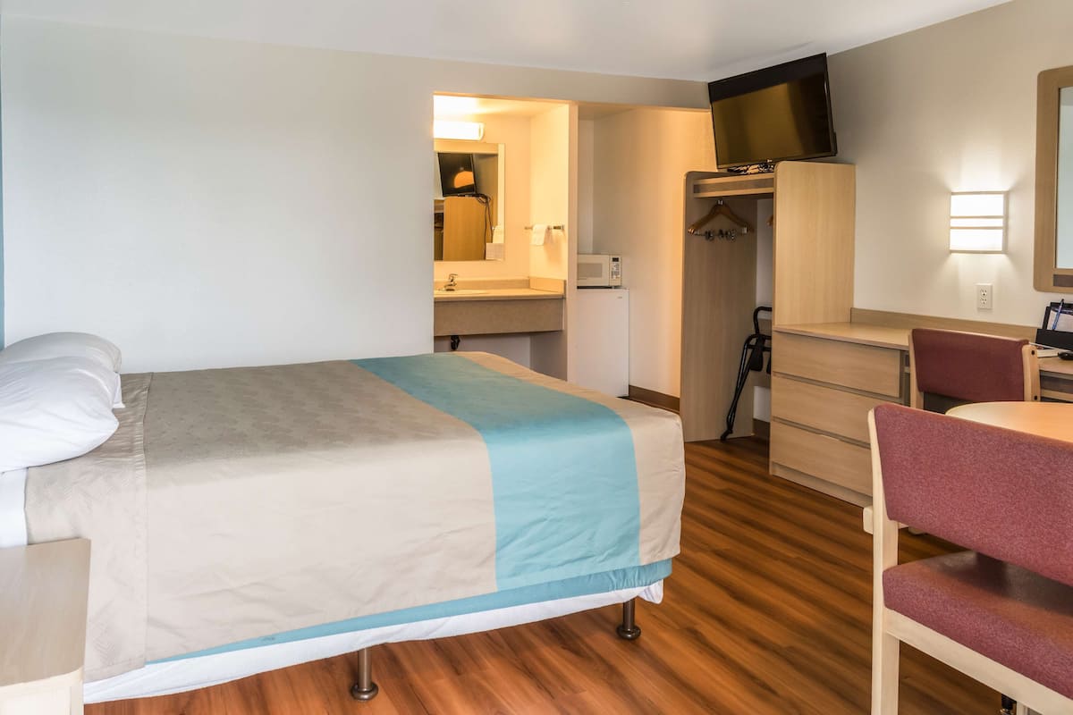 A hotel room with a bed, a desk, a chair, a microwave, and a closet.