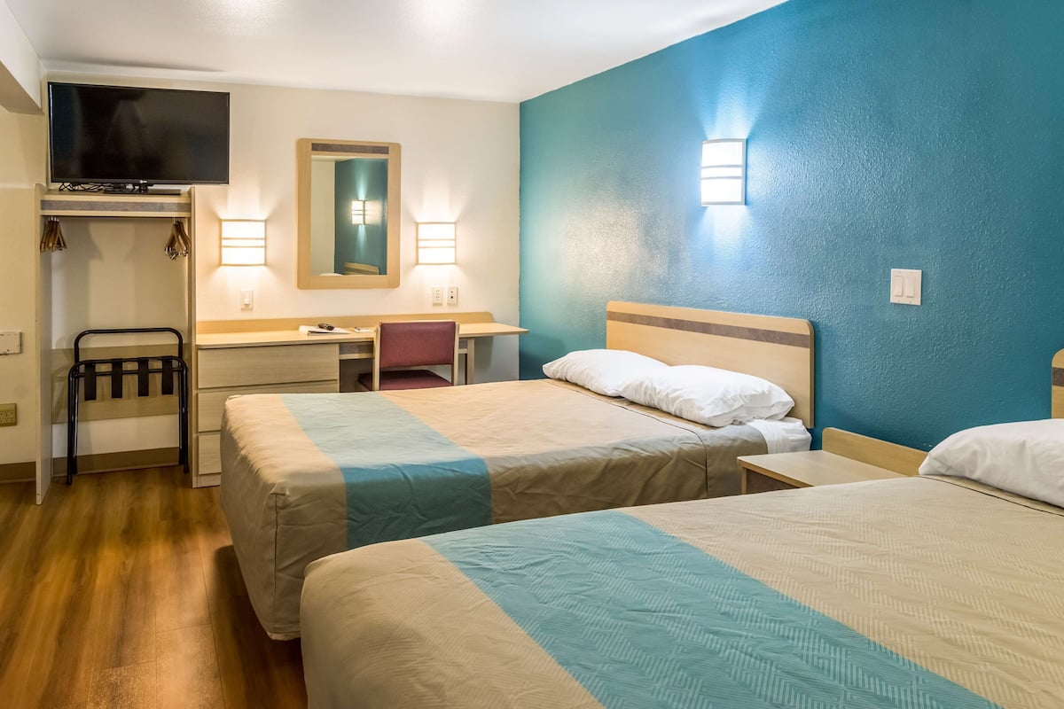 A hotel room with two beds, a desk, a chair, a TV, and two wall-mounted lights.