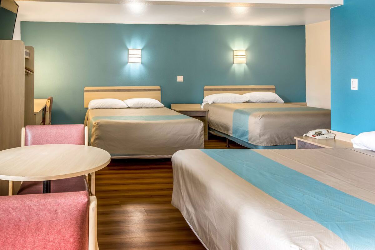 A hotel room with two beds, a small table, and a chair.
