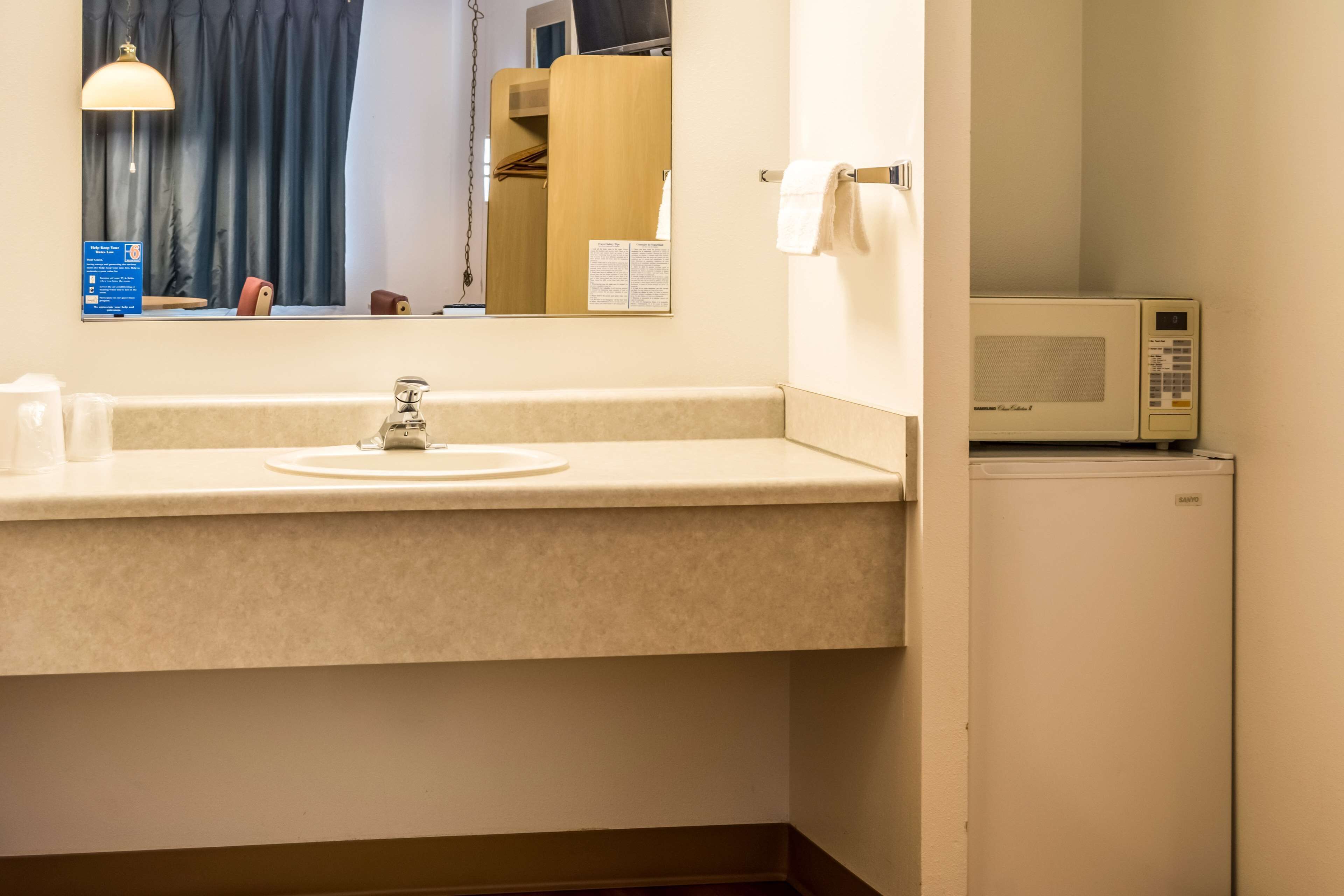 Um banheiro de hotel com pia, espelho e micro-ondas.