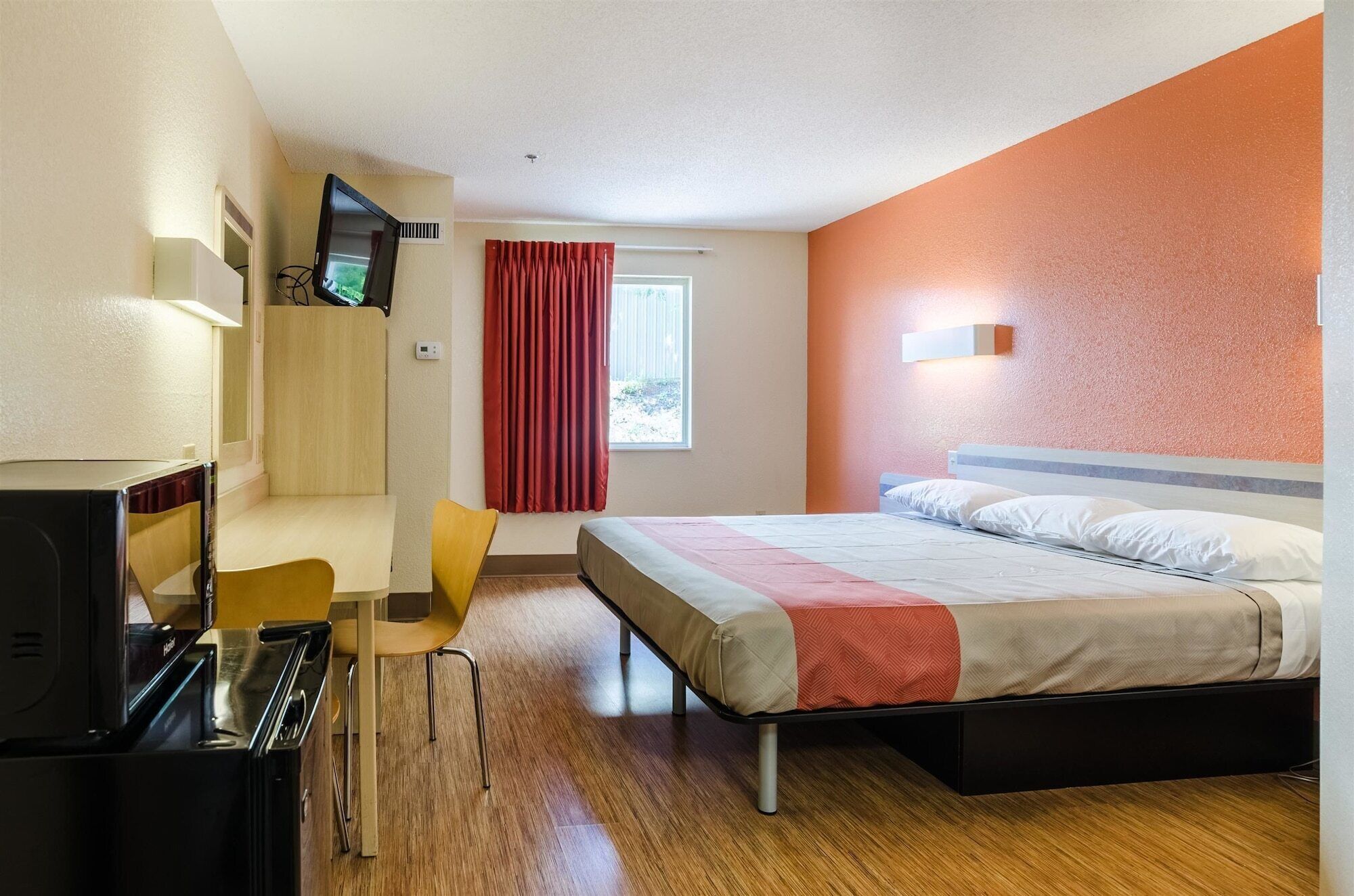 A hotel room with a bed, a desk with a chair, a television, and a window with curtains.