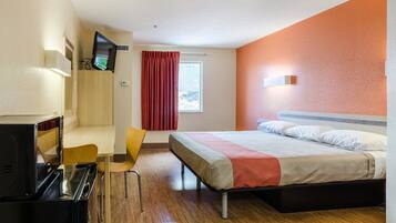 A hotel room with a bed, a desk with a chair, a television, and a window with curtains.