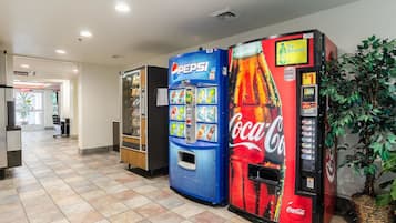 A vending area with Pepsi and Coca-Cola machines, a plant, and a sign for an elevator.