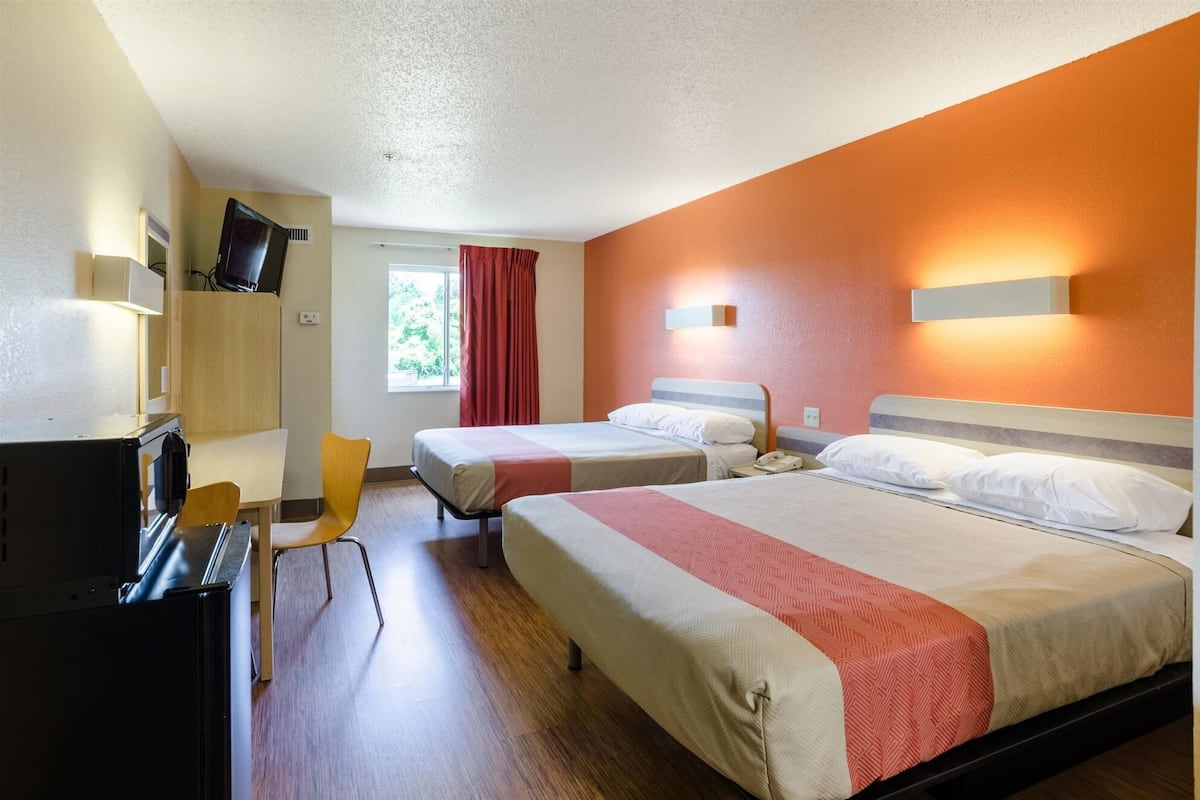 A hotel room with two beds, a desk, a chair, and a television.