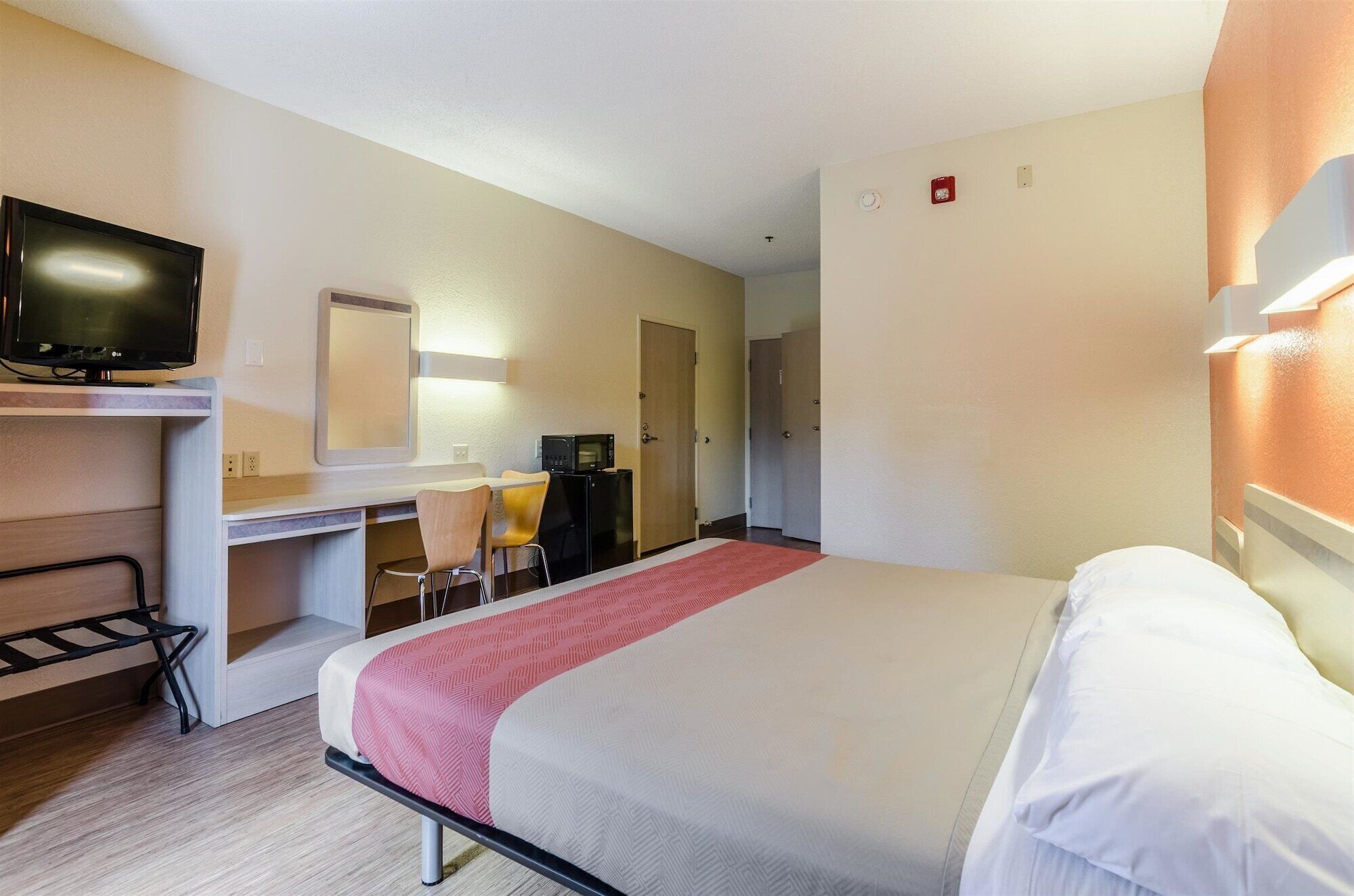 Una habitación de hotel con una cama, un escritorio con una silla, un televisor y un microondas.