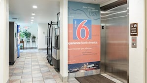 A hallway with a large promotional poster for a motel, an elevator, and a fire safety sign. - Motel 6 Bristol, VA (Bristol)