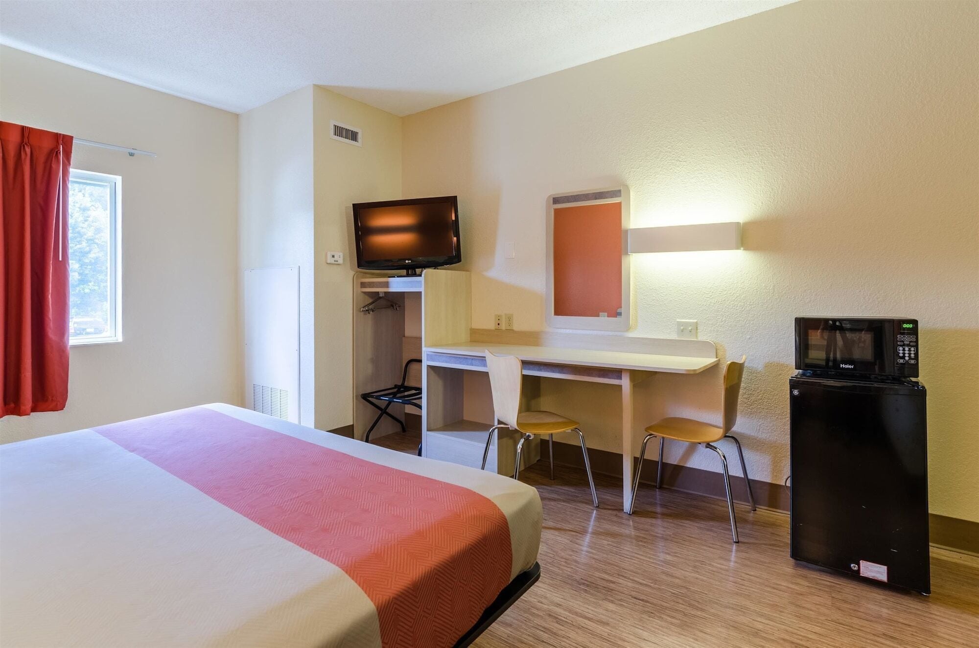 Une chambre d’hôtel équipée d’un lit, d’un bureau, de deux chaises, d’une télévision et d’un réfrigérateur.