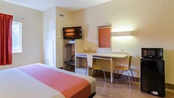 A hotel room with a bed, a desk, two chairs, a television, and a refrigerator.