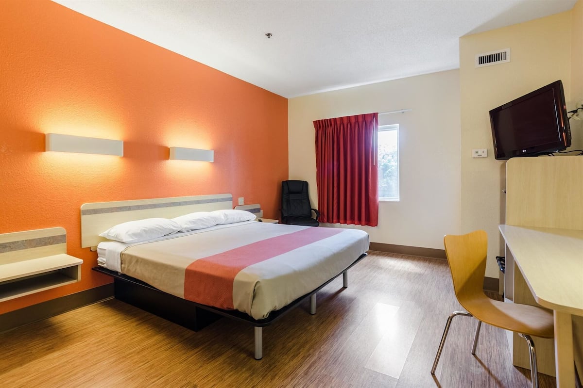 A hotel room with a bed, a desk, a chair, a TV, and a window with curtains.