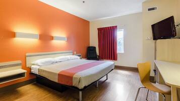 A hotel room with a bed, a desk, a chair, a TV, and a window with curtains.