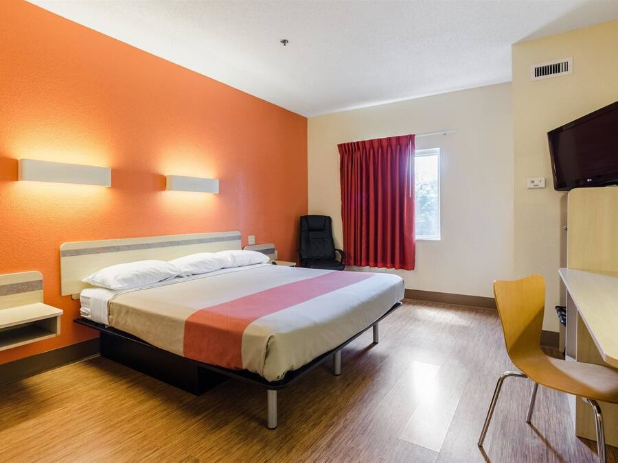 A hotel room with a bed, a desk, a chair, a TV, and a window with curtains.