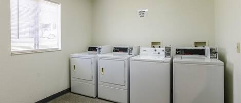 A laundry room with three stacked washers and dryers, a window with blinds, and a sign indicating the cost of using the washer and dryer.