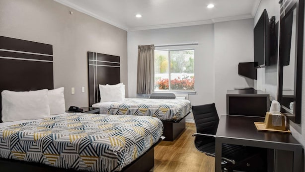 Une chambre d’hôtel avec deux lits, un bureau, une chaise, une télévision et une fenêtre avec des rideaux.