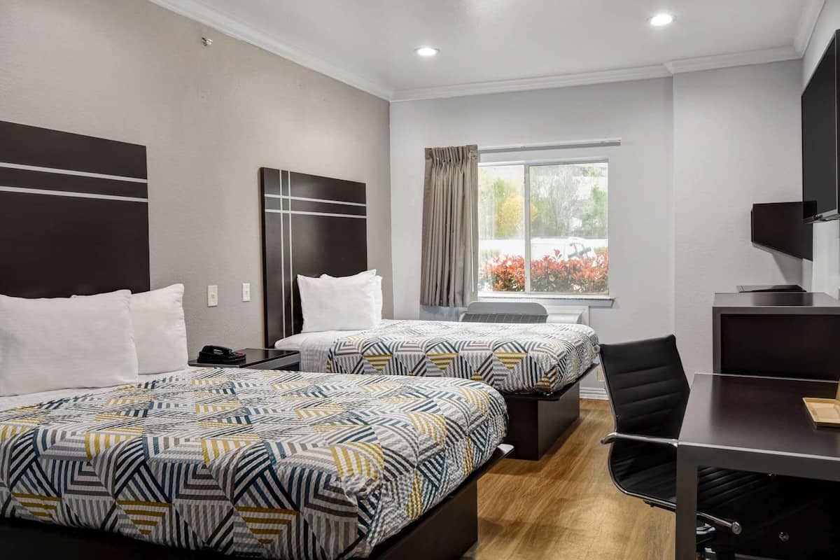 A hotel room with two beds, a desk, a chair, a TV, and a window with curtains.