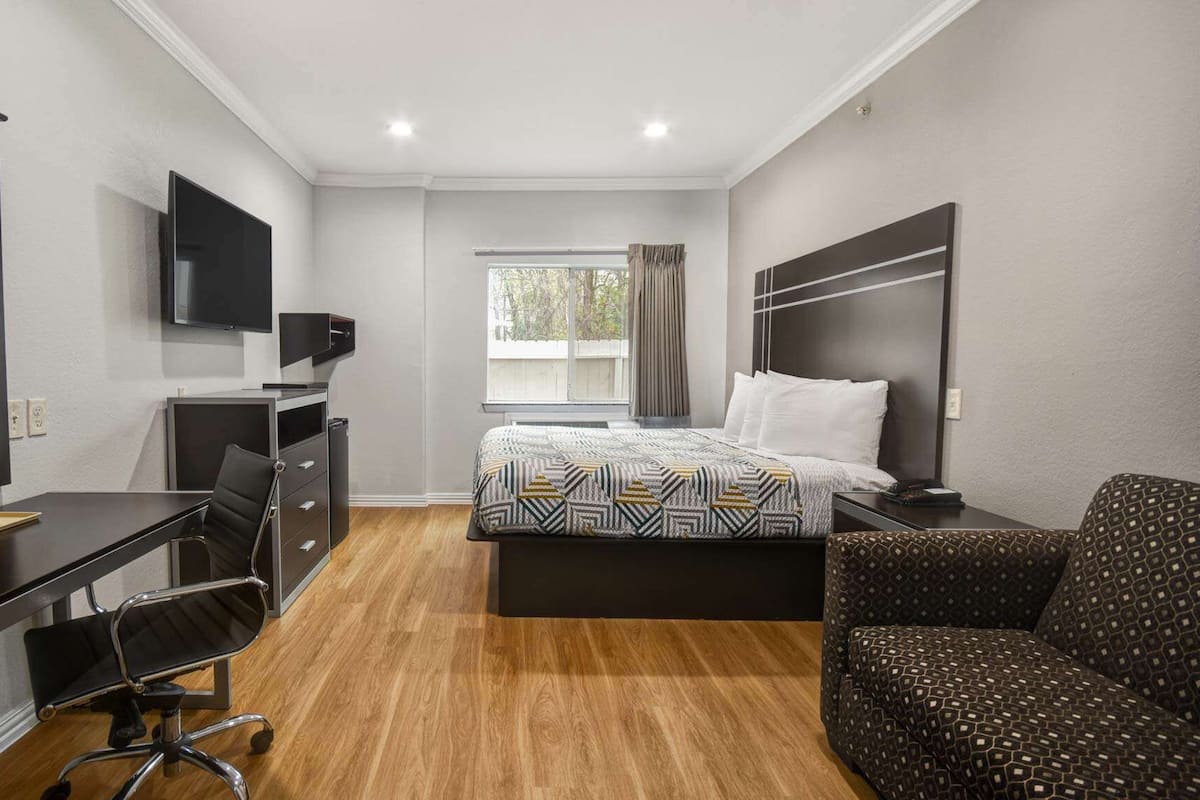 A hotel room with a bed, a desk, a chair, a TV, and a window.