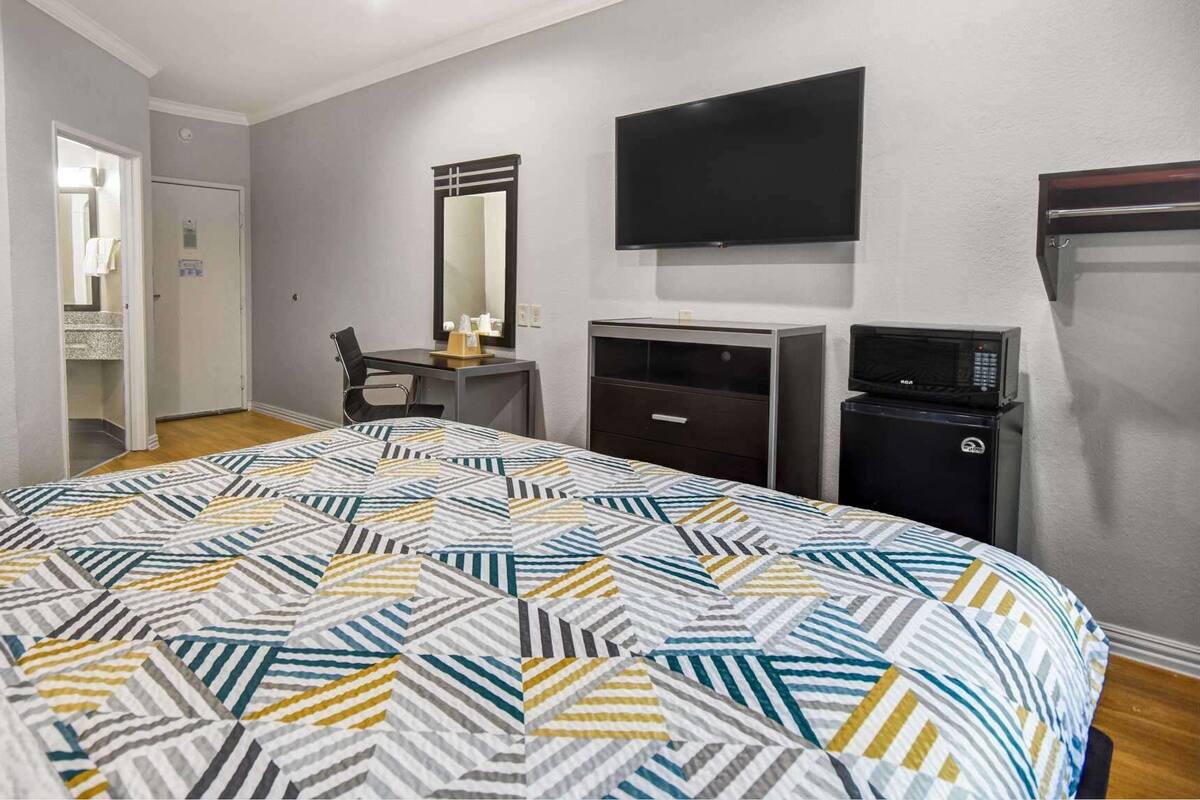 A hotel room with a large bed, a desk with a chair, a television, a microwave, and a door leading to a bathroom.