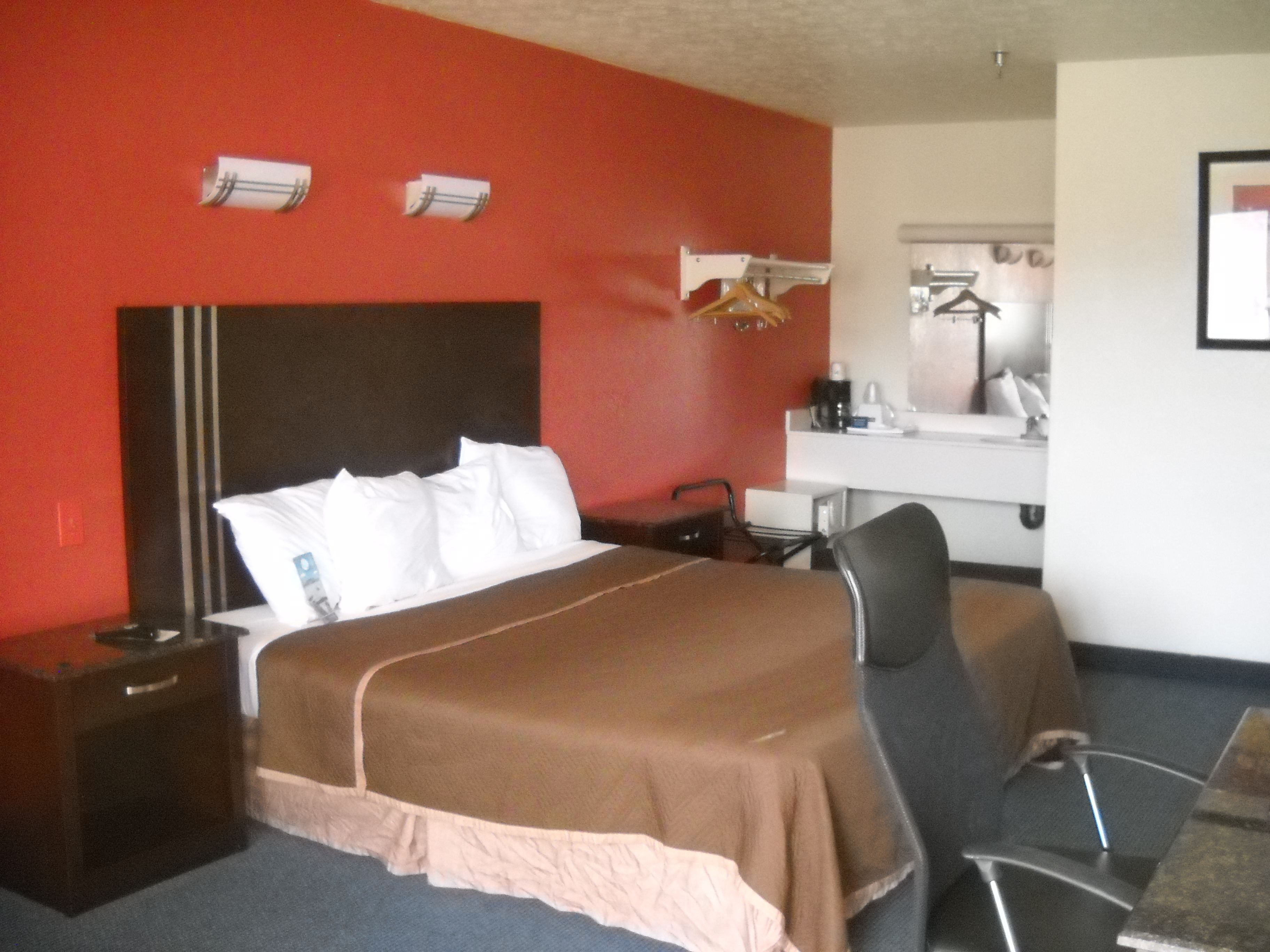 A hotel room with a bed, a desk, a chair, a nightstand, and a mirror.